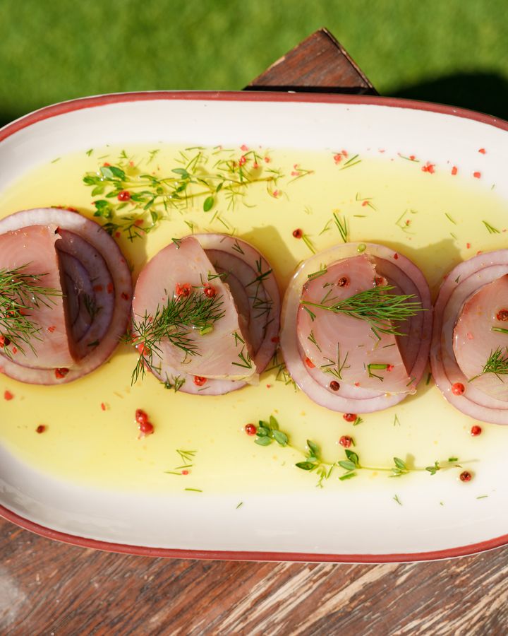 Ahşap tezgâhta oval tabakta soslu balık dilimleri ve kırmızı soğan
