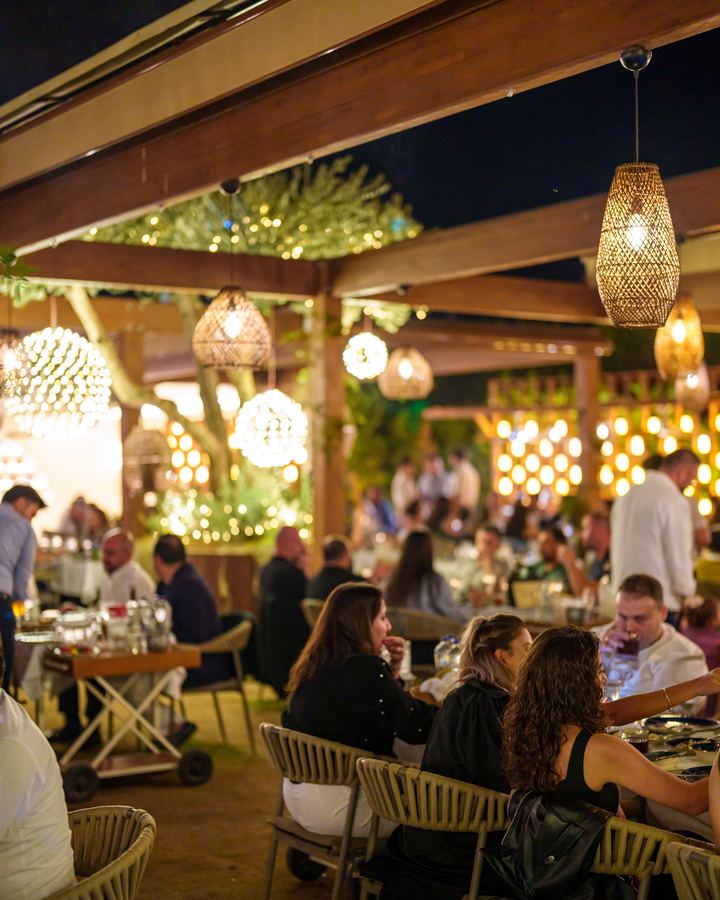 Gece pergola altında dolu masalar, hasır sarkıt avizeler ve ışıklı ağaçlar
